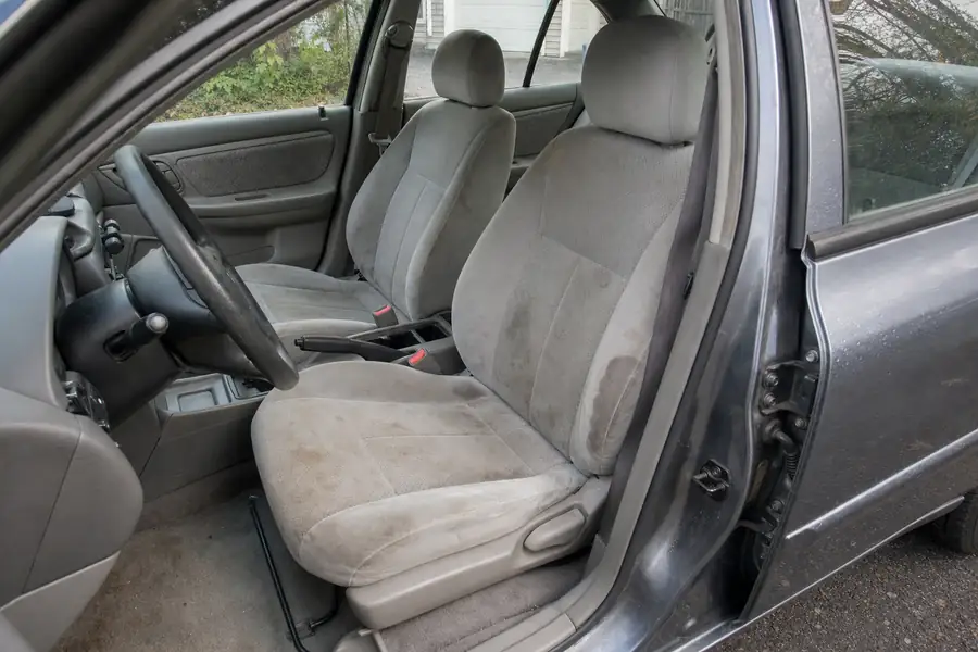 Car interior with visibly stained gray cloth seats, door open in a driveway