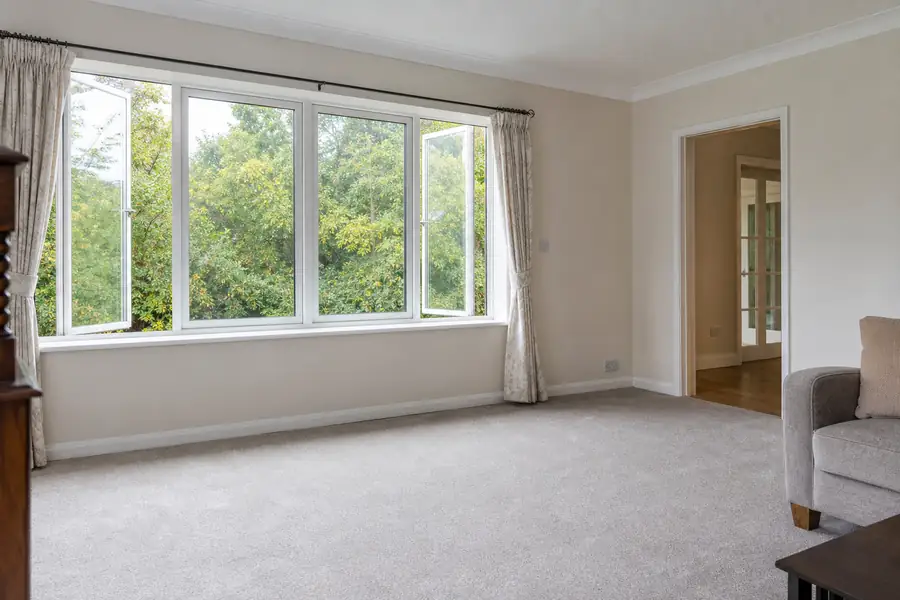 Wide-open windows airing out a bright living room with wall-to-wall carpet
