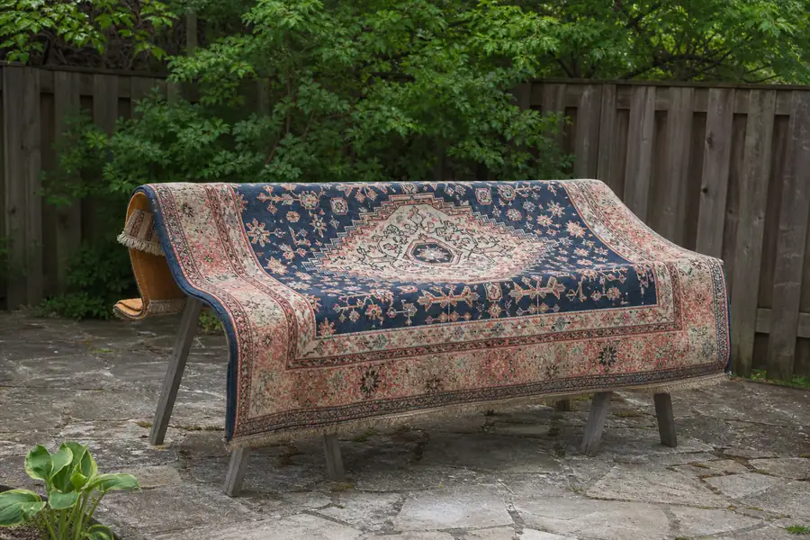 Area rug draped over sawhorses air-drying in a sunny backyard