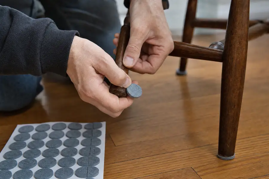 Person attaching felt pads under a wooden chair leg on a hardwood floor