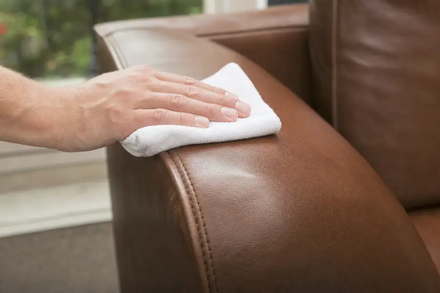 Hand wiping a leather couch armrest with a barely damp white microfiber cloth