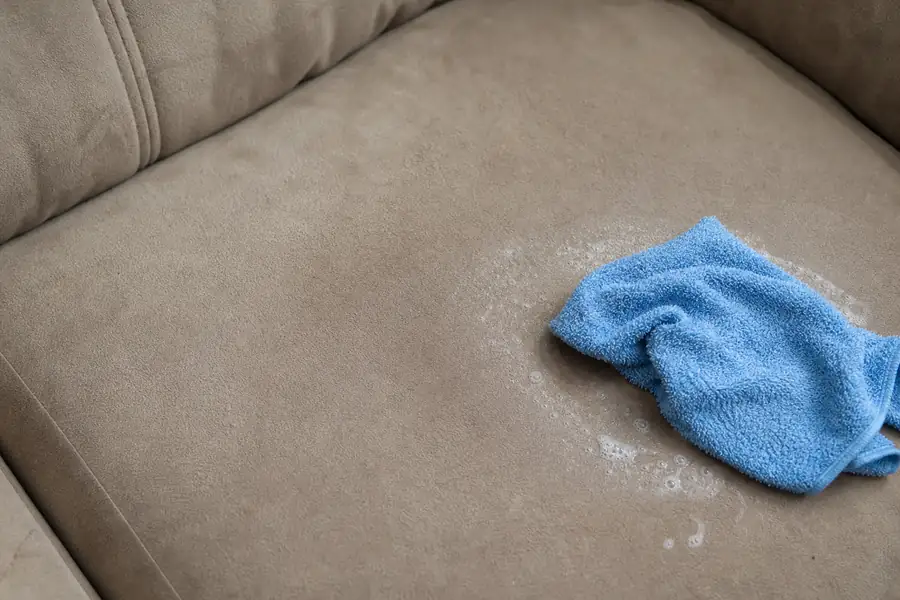 Microsuede sofa cushion being wiped clean with a damp cloth and mild soap