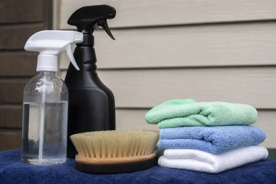 Upholstery cleaning tools arranged on a cloth: soft brush, microfiber towels, spray bottles