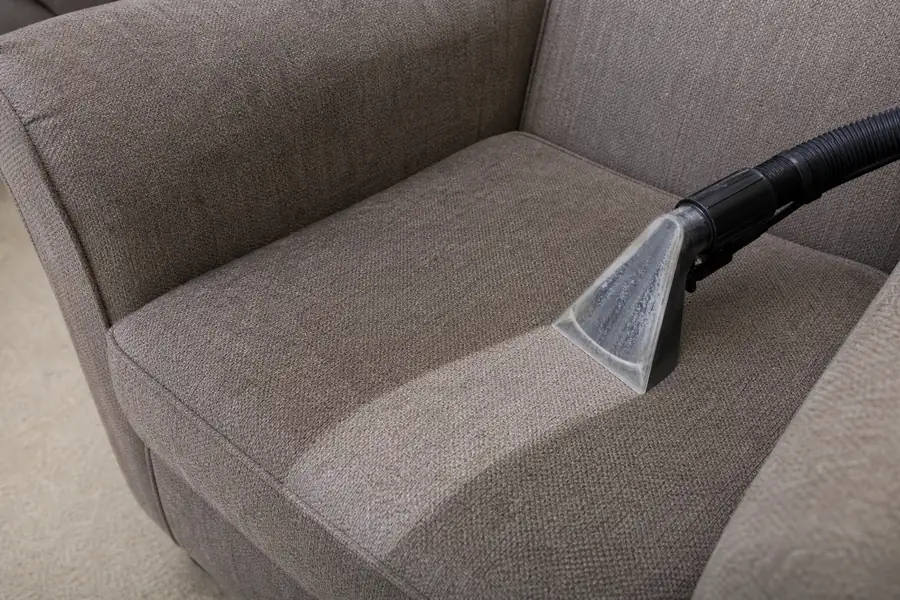 Upholstery extractor nozzle cleaning a fabric armchair seat with a visibly cleaner streak
