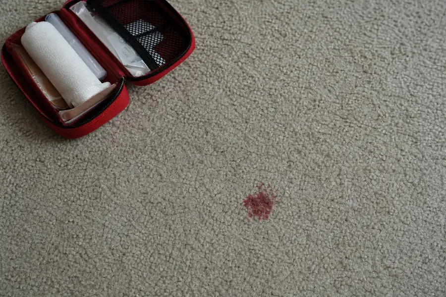 Small red stain on light beige carpet with a first aid kit nearby