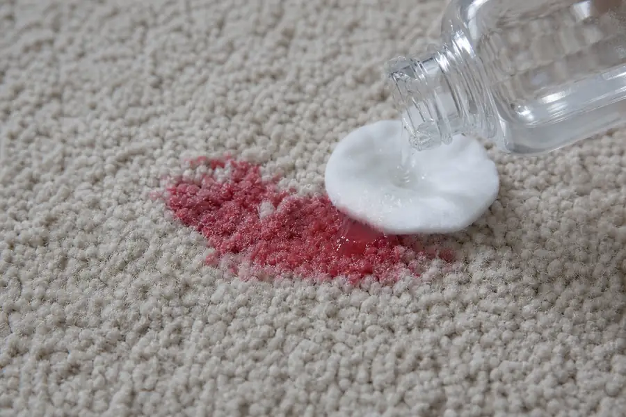 Cotton pad dabbing a red polish stain on carpet with clear solvent