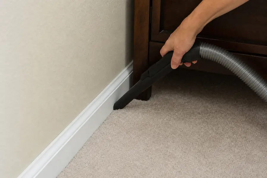 Person vacuuming along baseboards and carpet edges with a crevice attachment