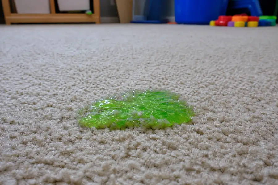 Bright green slime blob stuck in beige carpet fibers in a kids playroom