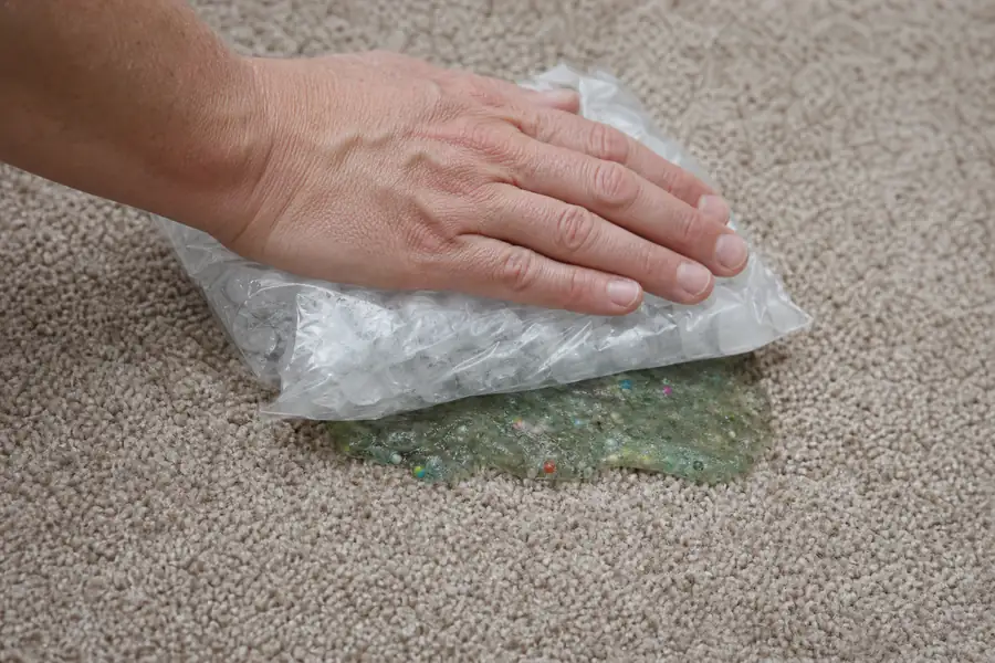 Hand pressing a bag of ice cubes onto slime in carpet to harden it