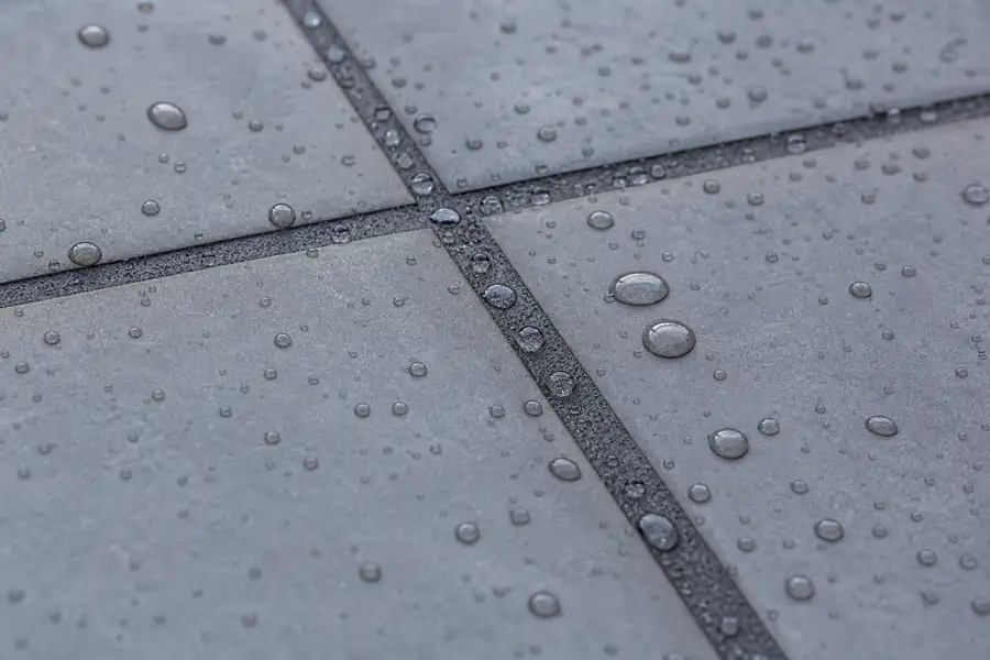 Water beading up on freshly sealed dark gray grout between porcelain tiles