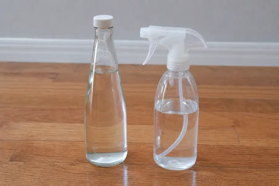 Glass bottle of white vinegar and a spray bottle standing on a hardwood floor