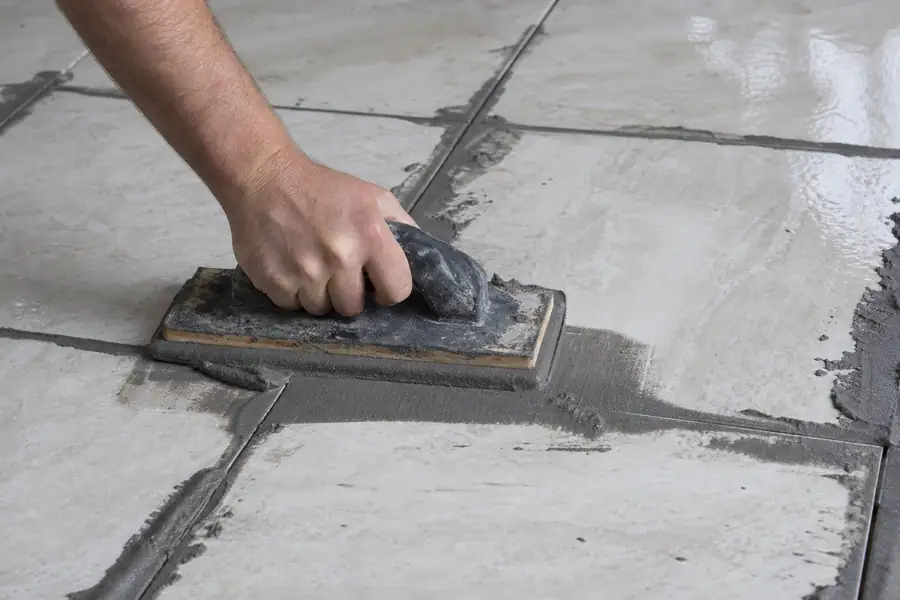 Tiler pressing fresh gray grout between ceramic tiles with a rubber float