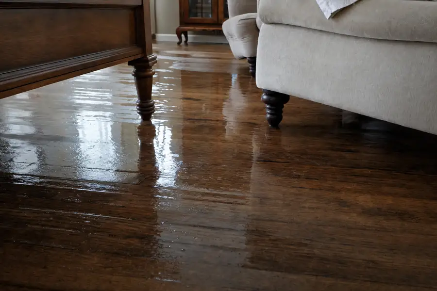 Water spreading across a hardwood living room floor from a burst pipe, furniture legs standing in water